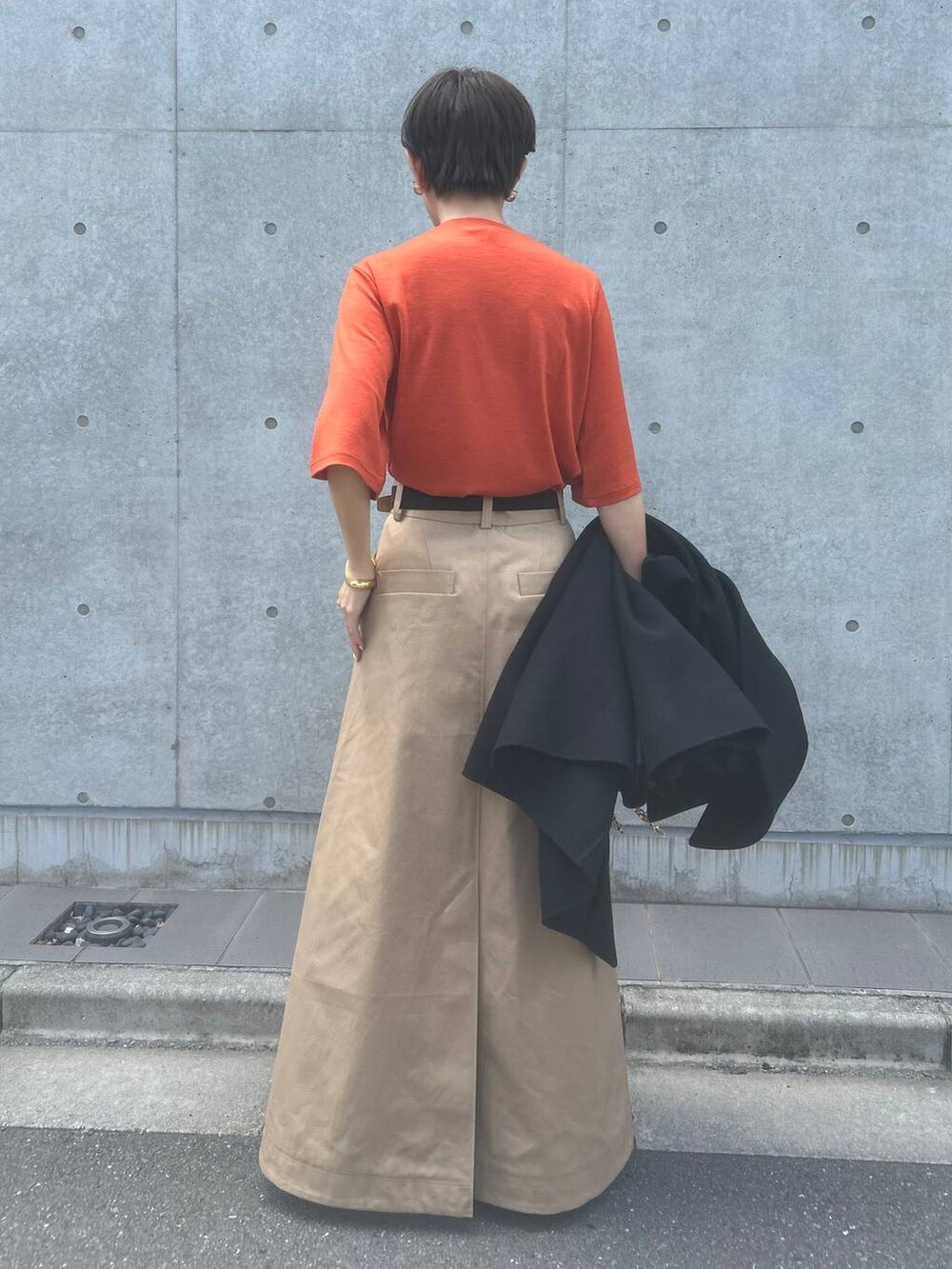 オレンジ系のTシャツ/カットソー、ベージュ系のスカート、ブラック系のその他アウターを着用したレディースの秋コーディネートの7枚目の写真