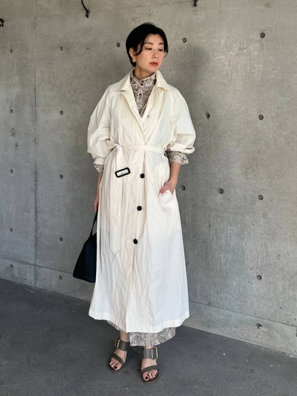 ホワイト系のステンカラーコート、ベージュ系のワンピースを着用したレディースの春コーディネートの2枚目の写真