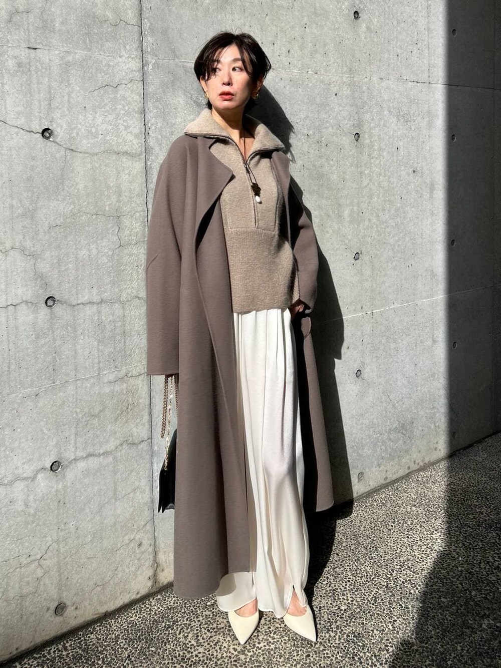 ブラウン系のノーカラーコート、ホワイト系のその他パンツ、ベージュ系のニット/セーターを着用したレディースの冬コーディネートの2枚目の写真