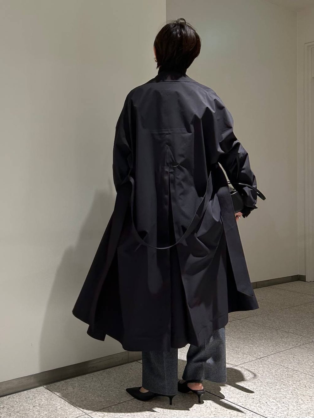 ブラック系のニット/セーター、ブラック系のトレンチコート、グレー系のスラックスを着用したレディースの秋コーディネートの3枚目の写真