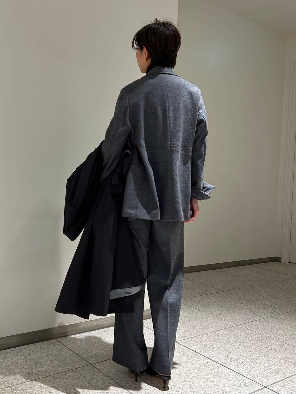 ブラック系のニット/セーター、ブラック系のトレンチコート、グレー系のスラックスを着用したレディースの秋コーディネートの5枚目の写真