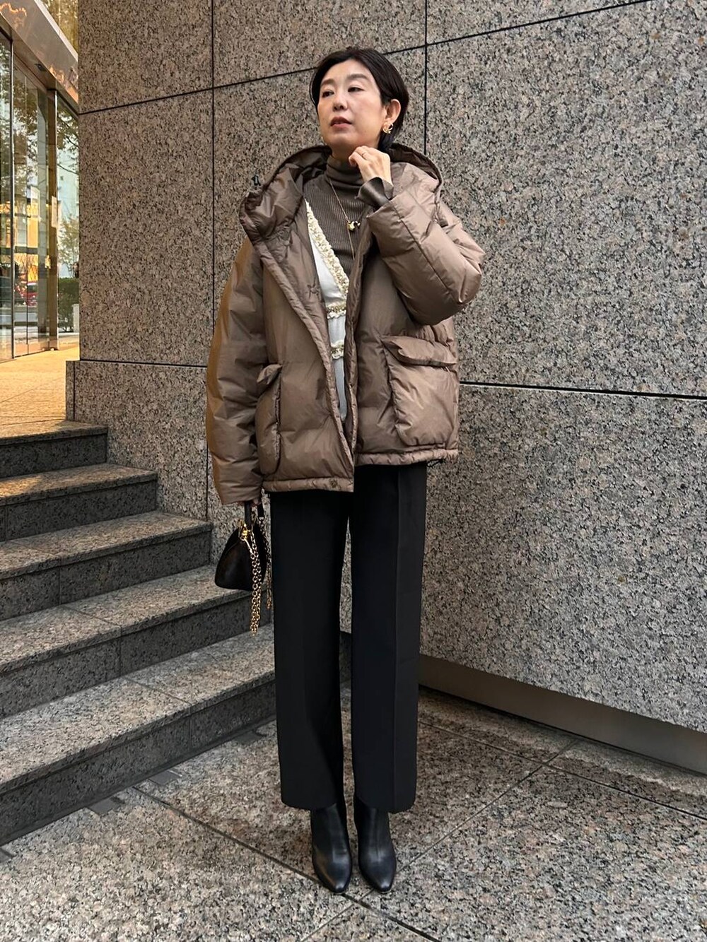 ベージュ系のニット/セーター、ブラウン系のダウンジャケット/コート、ブラック系のスラックスを着用したレディースの冬コーディネートの2枚目の写真