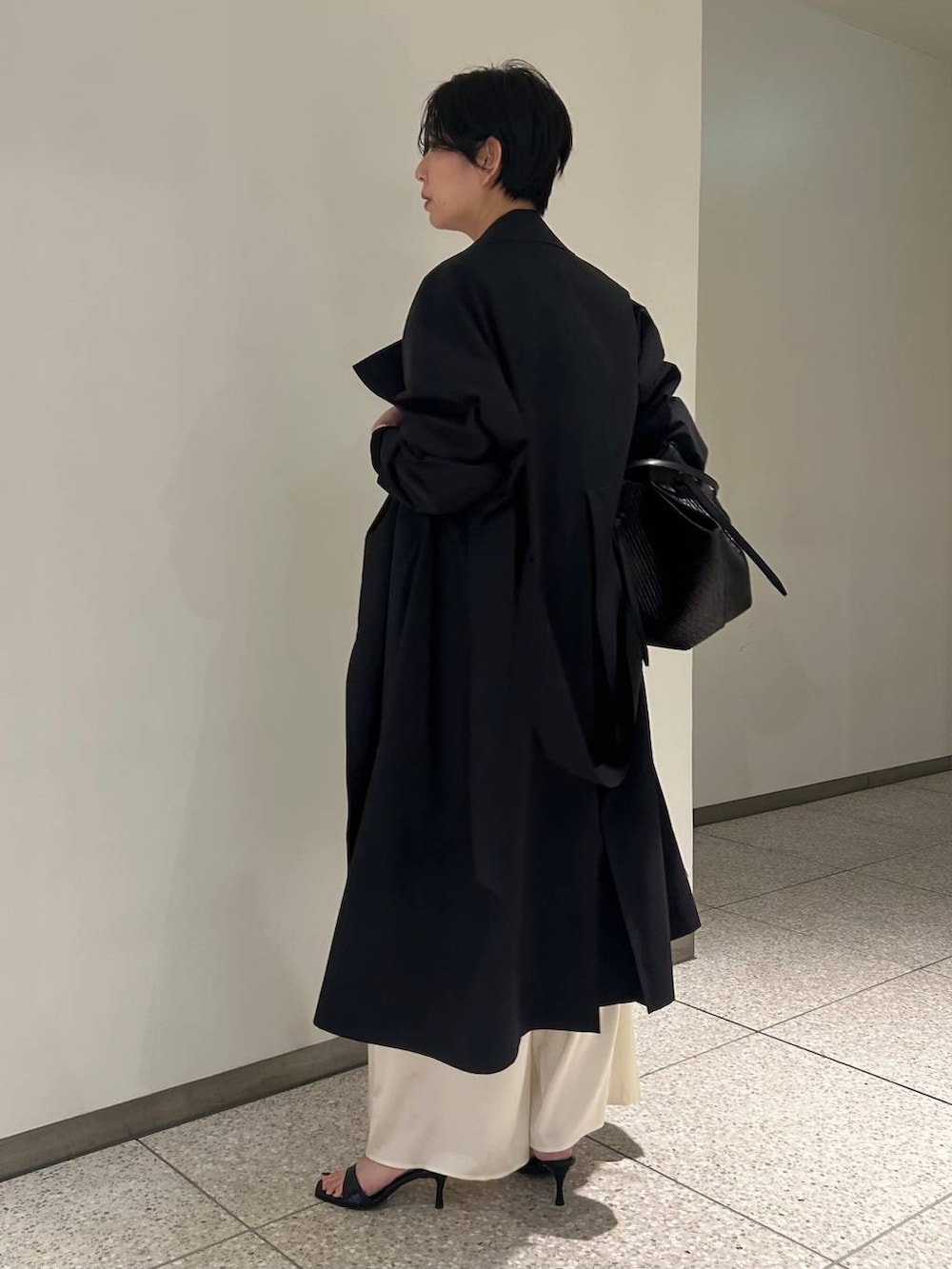 ホワイト系のニット/セーター、ホワイト系のシャツ/ブラウス、ブラック系のトレンチコートを着用したレディースの冬コーディネートの2枚目の写真