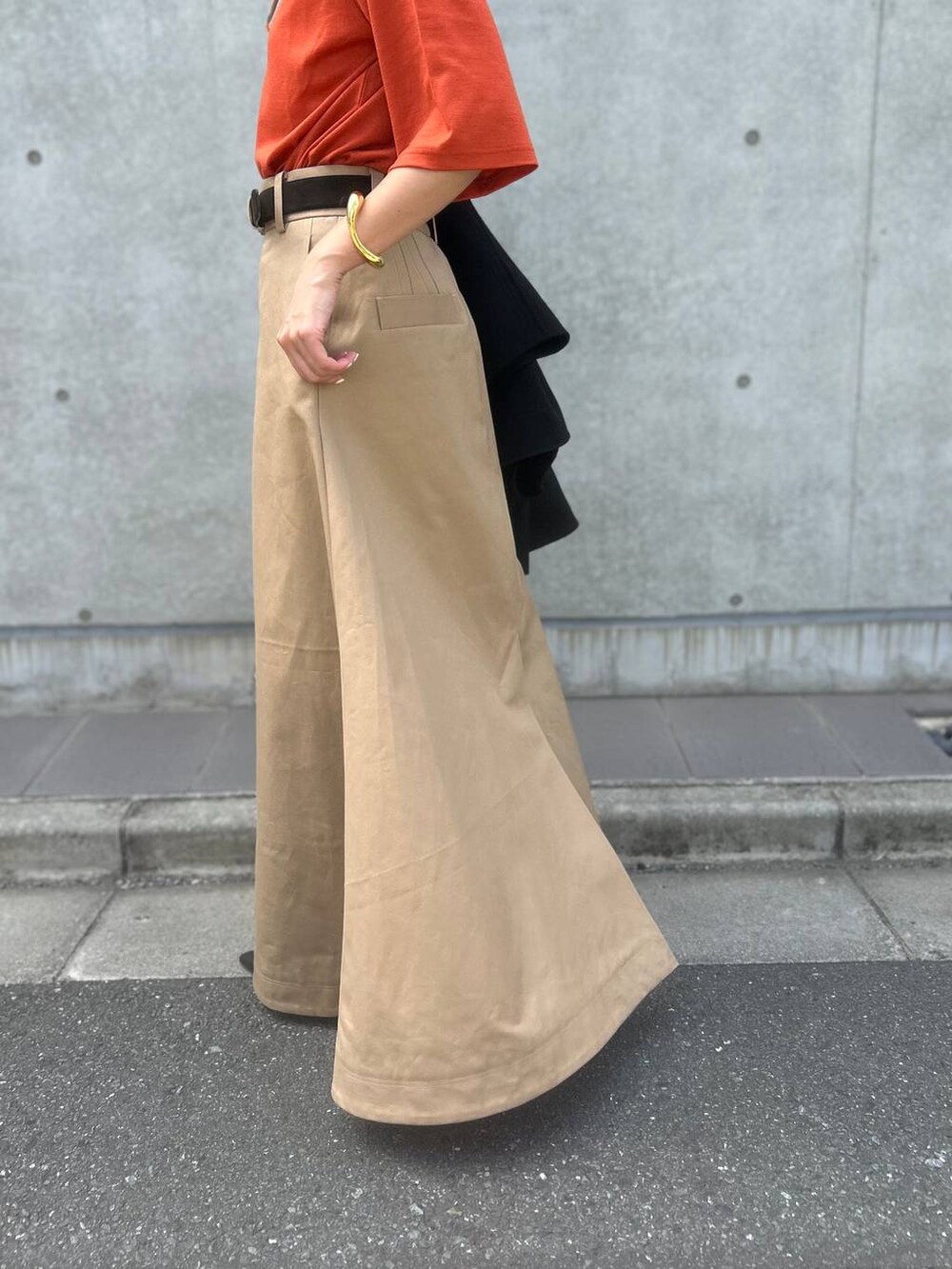 オレンジ系のTシャツ/カットソー、ベージュ系のスカート、ブラック系のその他アウターを着用したレディースの秋コーディネートの9枚目の写真