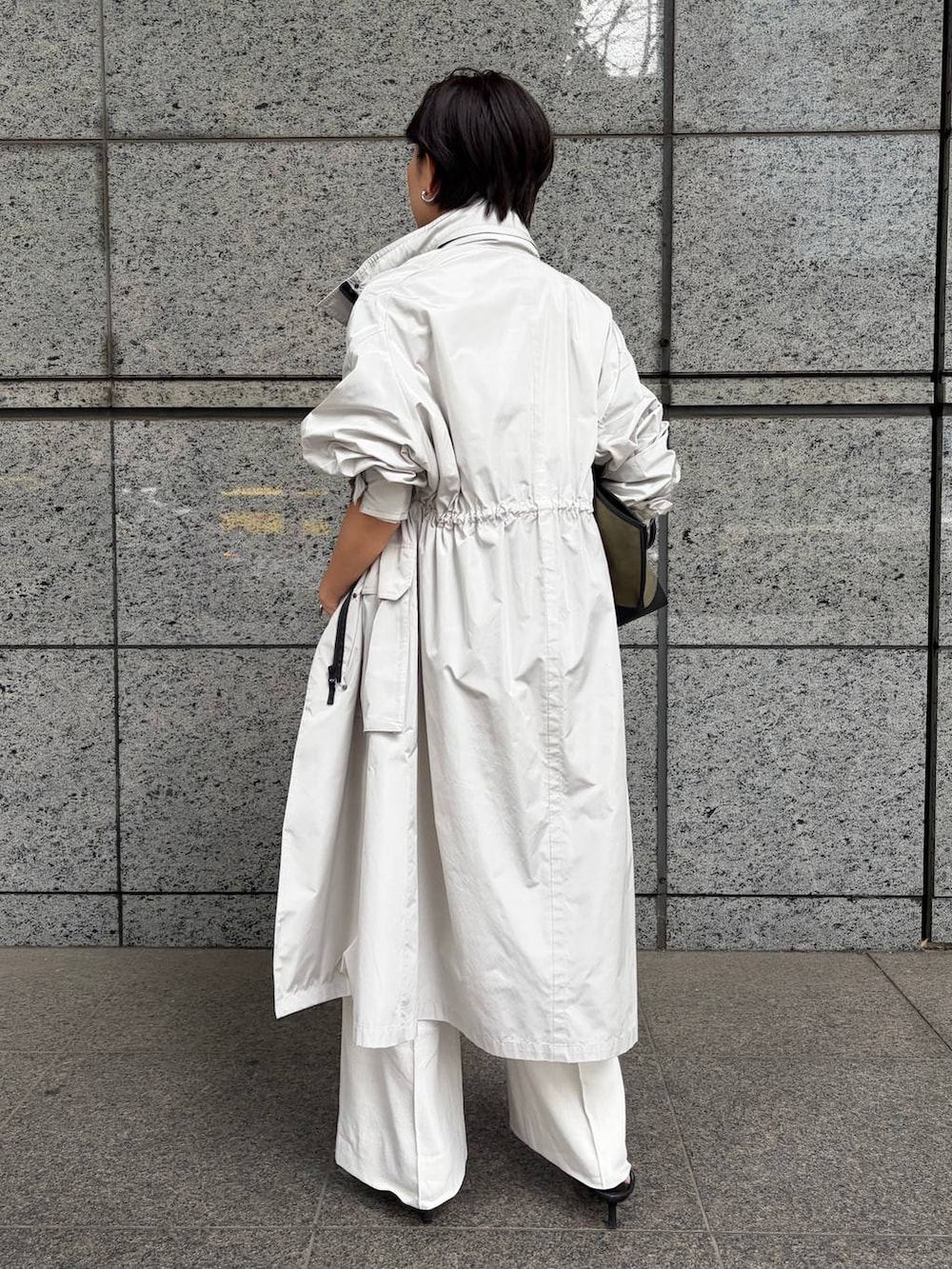 グリーン系のニット/セーター、ホワイト系のスラックス、グレー系のナイロンジャケットを着用したレディースの春コーディネートの3枚目の写真