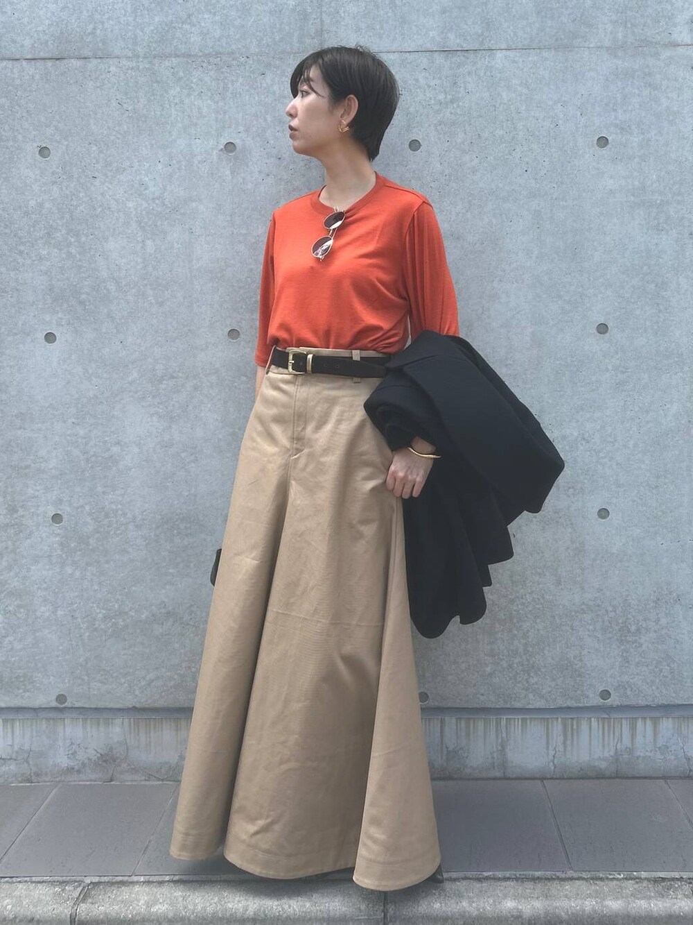 オレンジ系のTシャツ/カットソー、ベージュ系のスカート、ブラック系のその他アウターを着用したレディースの秋コーディネートの6枚目の写真