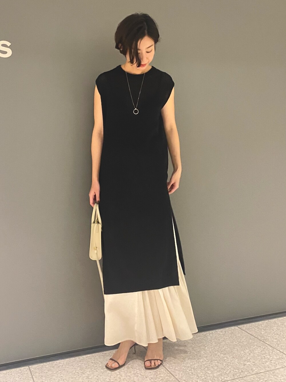 ブラック系のベスト、ベージュ系のスカート、ブラウン系のサンダルを着用したレディースの春コーディネートの2枚目の写真