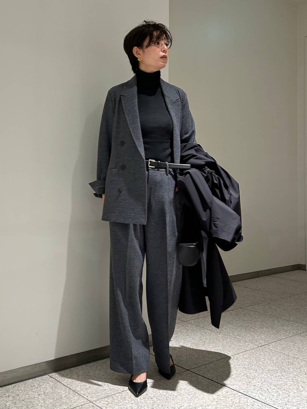 ブラック系のニット/セーター、ブラック系のトレンチコート、グレー系のスラックスを着用したレディースの秋コーディネートの4枚目の写真
