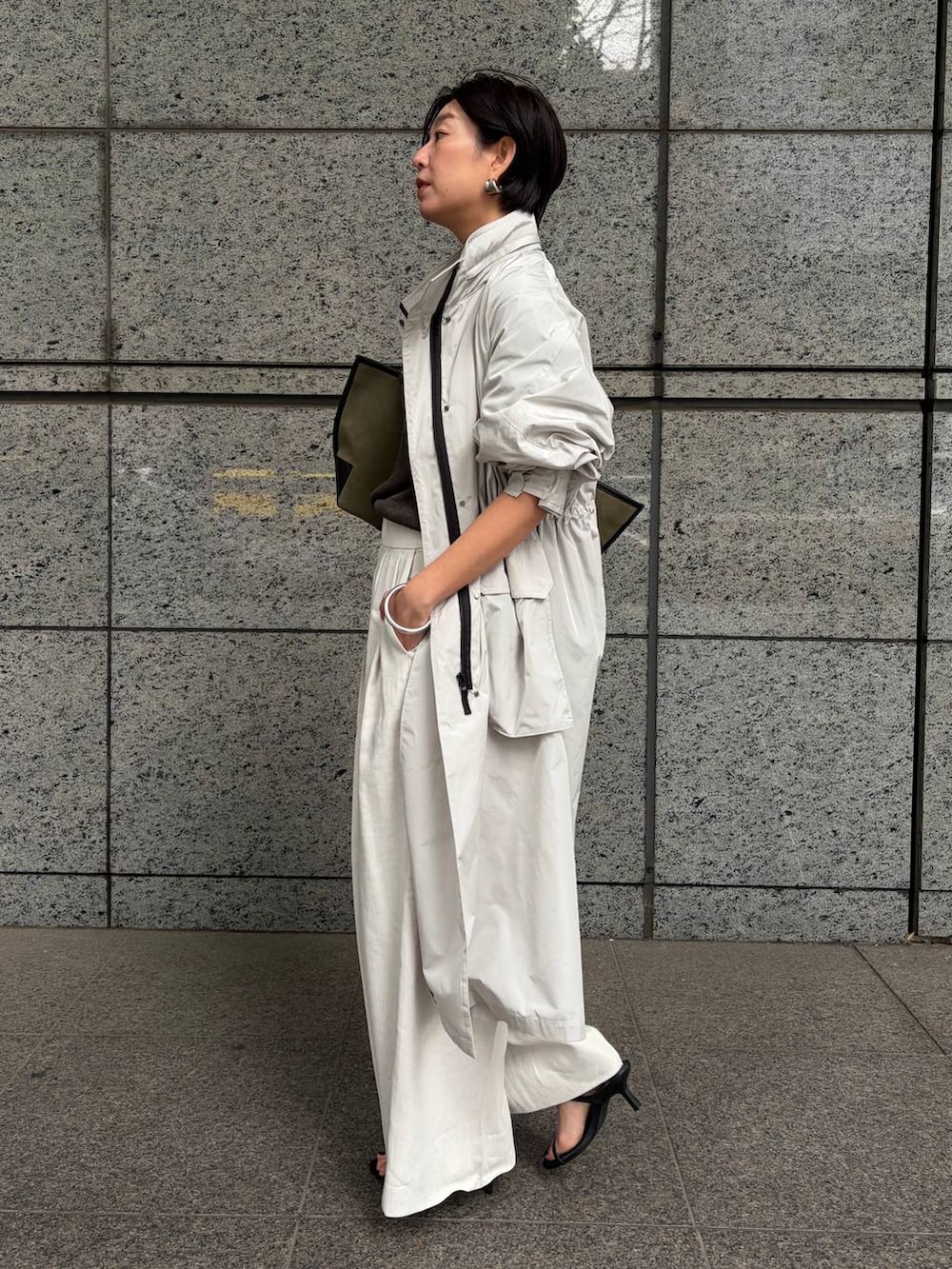 グリーン系のニット/セーター、ホワイト系のスラックス、グレー系のナイロンジャケットを着用したレディースの春コーディネートの2枚目の写真