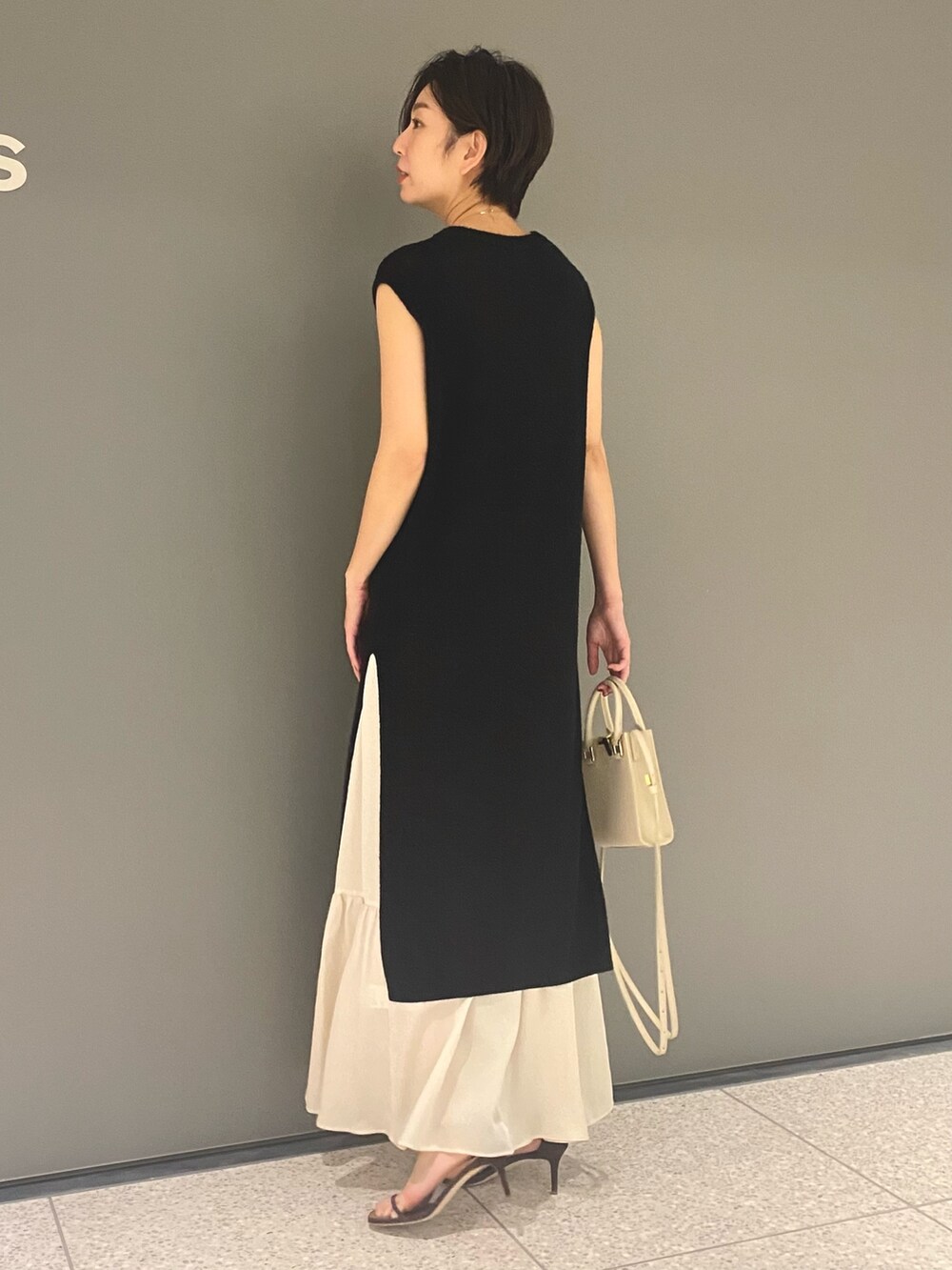 ブラック系のベスト、ベージュ系のスカート、ブラウン系のサンダルを着用したレディースの春コーディネートの3枚目の写真