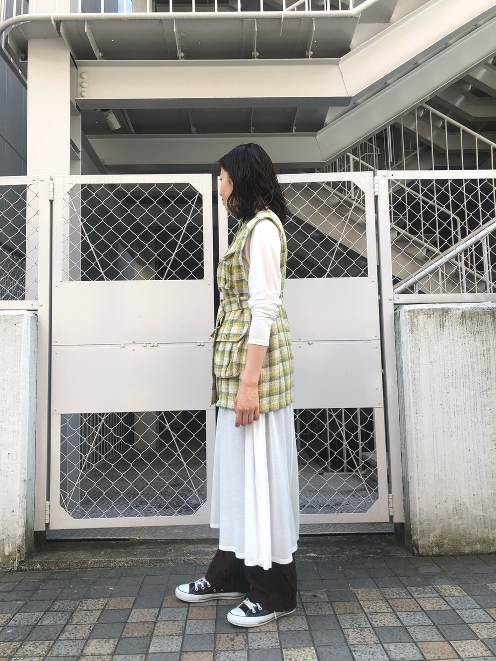 イエロー系のベスト、ホワイト系のワンピース、ブラウン系のその他パンツを着用したレディースの春コーディネートの2枚目の写真