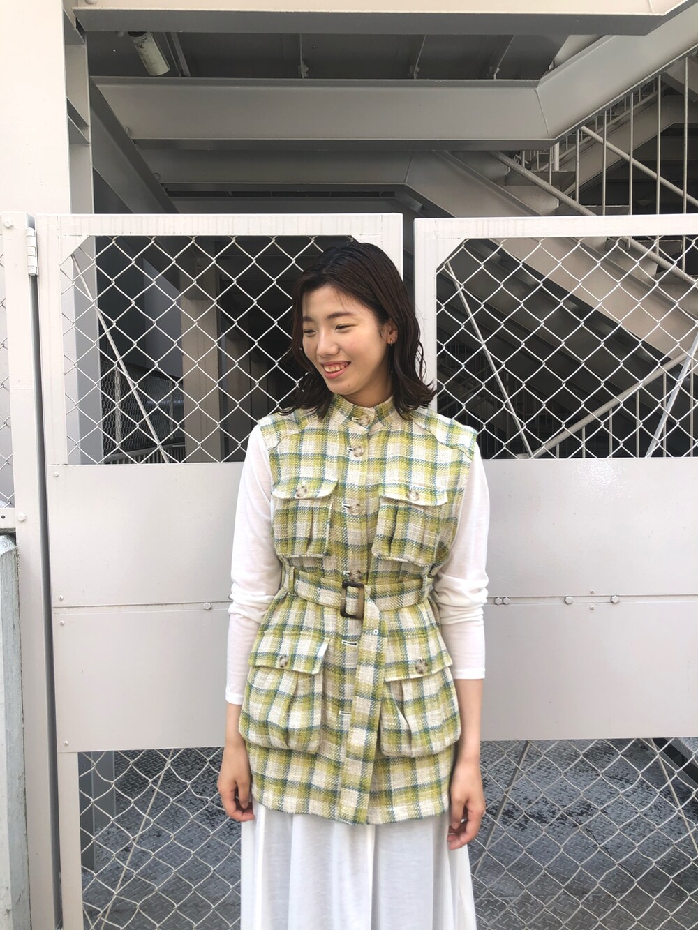 イエロー系のベスト、ホワイト系のワンピース、ブラウン系のその他パンツを着用したレディースの春コーディネートの3枚目の写真