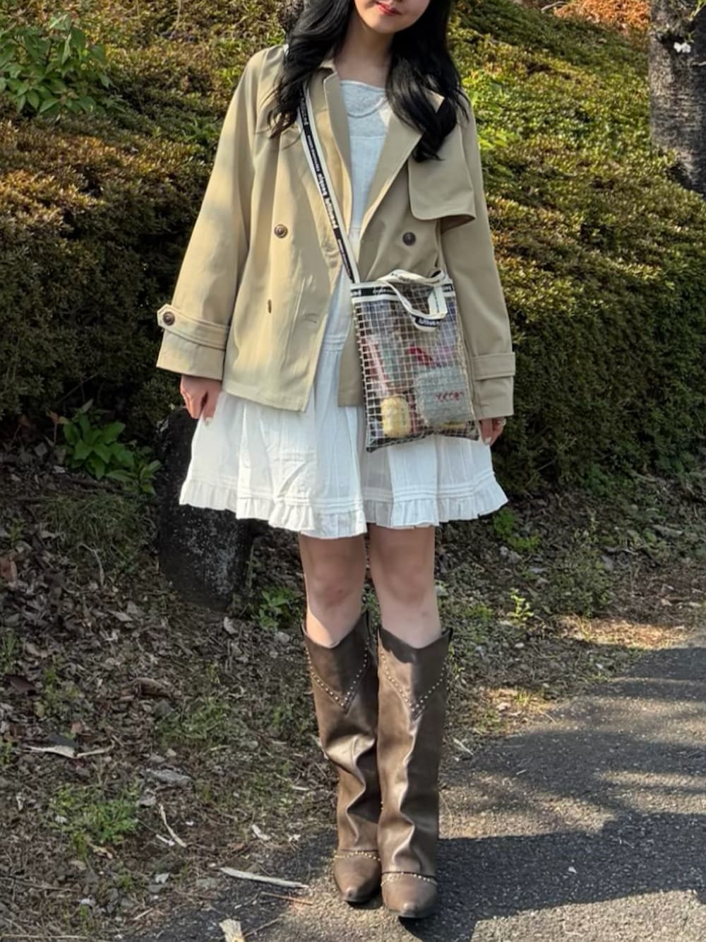 ベージュ系のトレンチコート、ホワイト系のワンピース、ブラック系のショルダーバッグを着用したレディースの春コーディネートの2枚目の写真