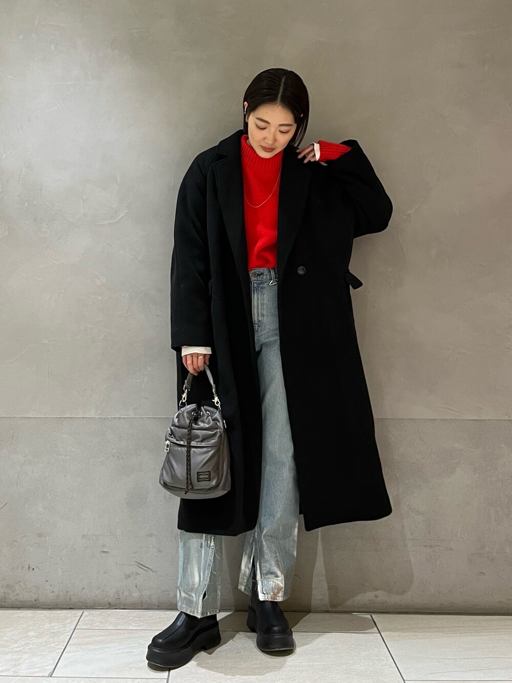 レッド系のニット/セーター、ブラック系のチェスターコート、ブルー系のデニムパンツを着用したレディースの冬コーディネートの2枚目の写真
