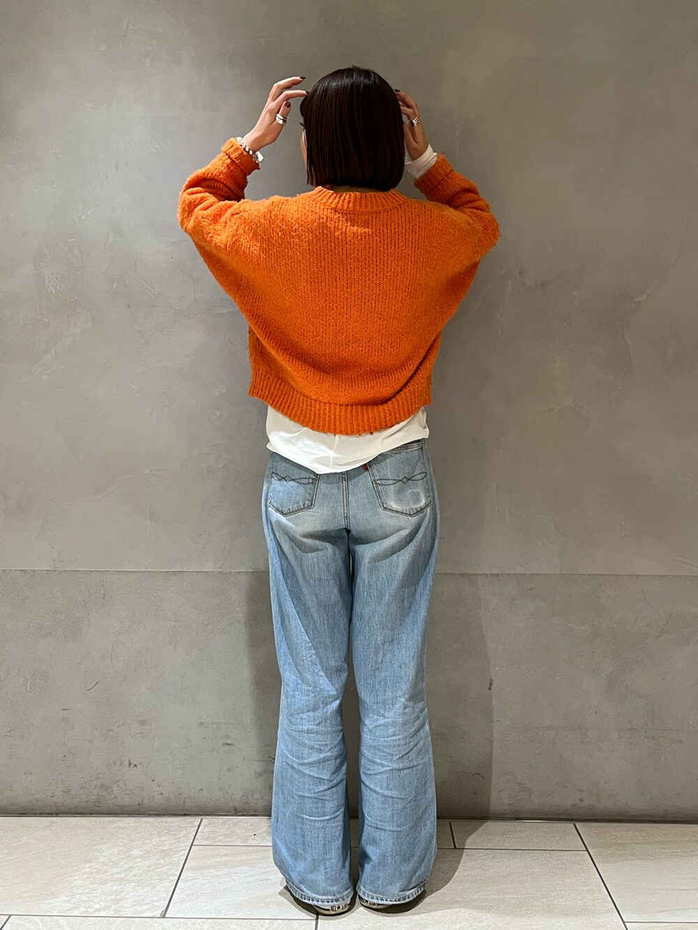 オレンジ系のニット/セーター、ブルー系のデニムパンツを着用したレディースの冬コーディネートの4枚目の写真