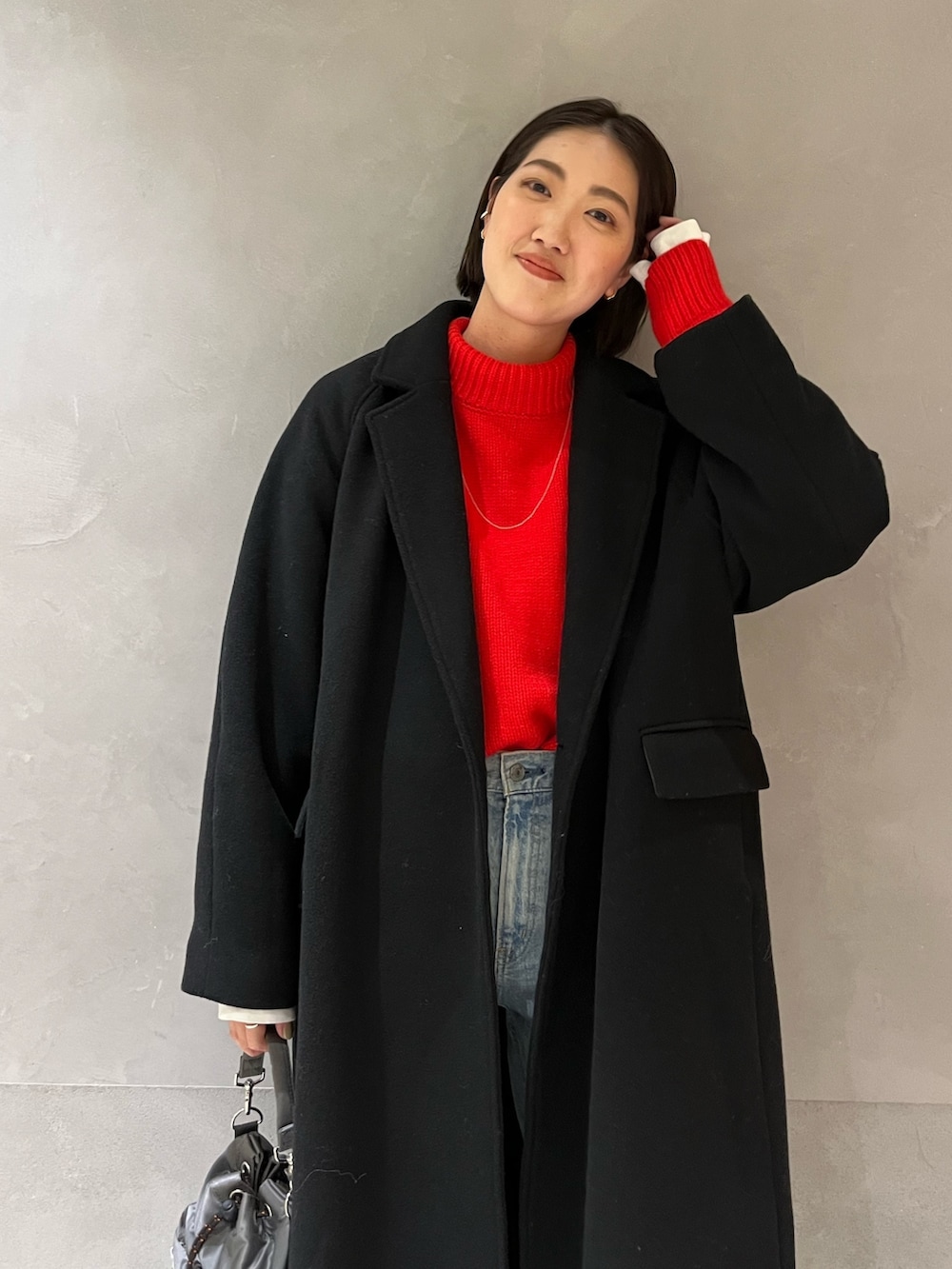 レッド系のニット/セーター、ブラック系のチェスターコート、ブルー系のデニムパンツを着用したレディースの冬コーディネートの3枚目の写真