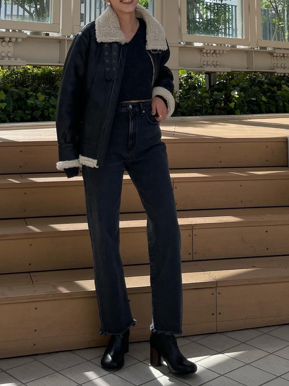 ブラック系のムートンコート、グレー系のニット/セーター、ブラック系のデニムパンツを着用したレディースの秋コーディネートの2枚目の写真