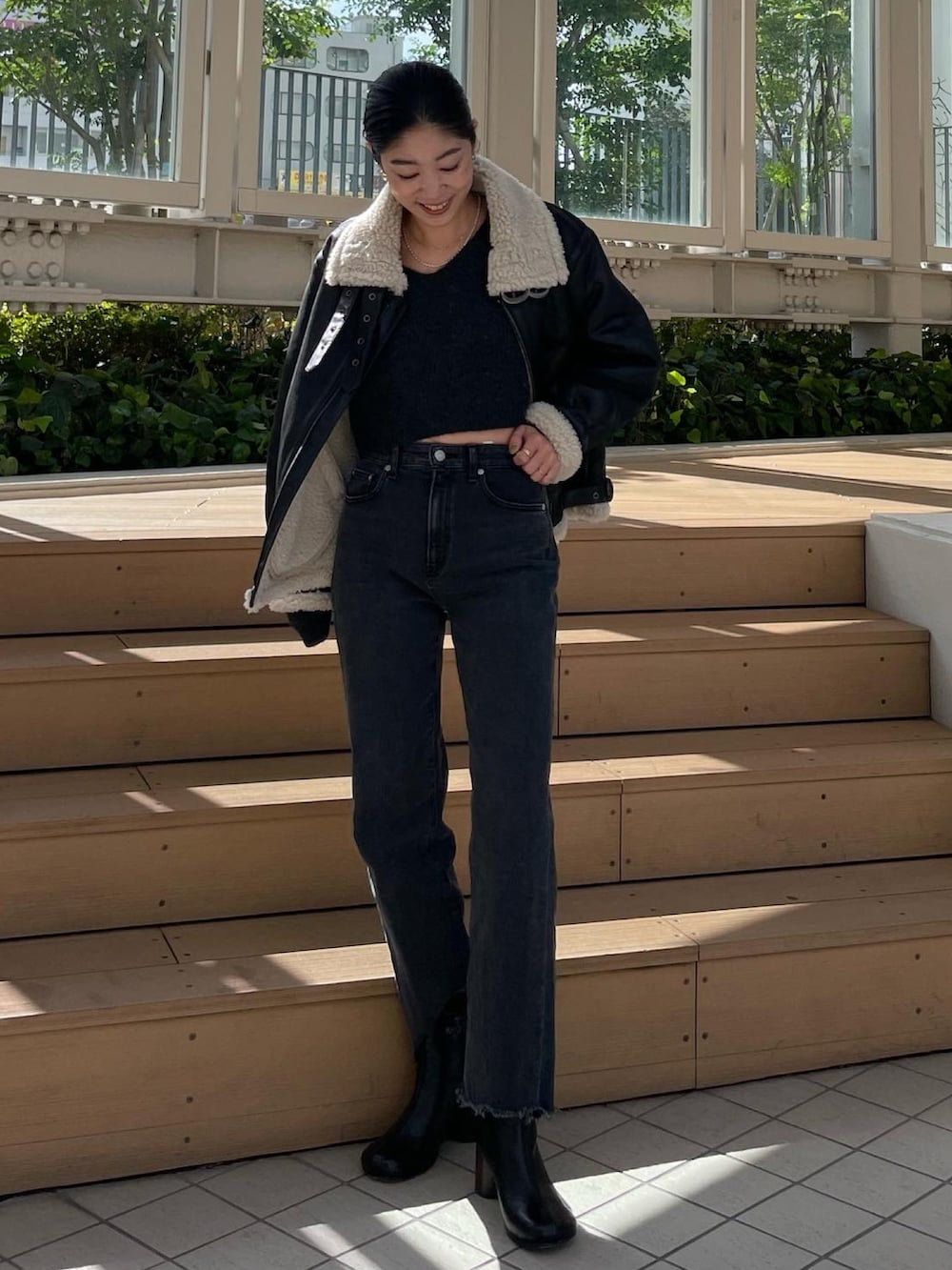 ブラック系のムートンコート、グレー系のニット/セーター、ブラック系のデニムパンツを着用したレディースの秋コーディネートの3枚目の写真