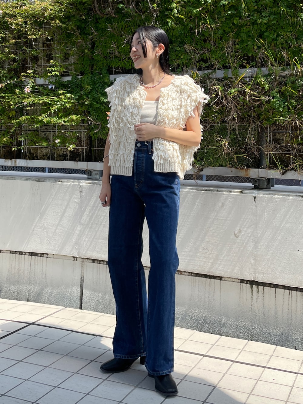 ブルー系のデニムパンツ、ホワイト系のベスト、ブラック系のブーツを着用したレディースの秋コーディネートの4枚目の写真