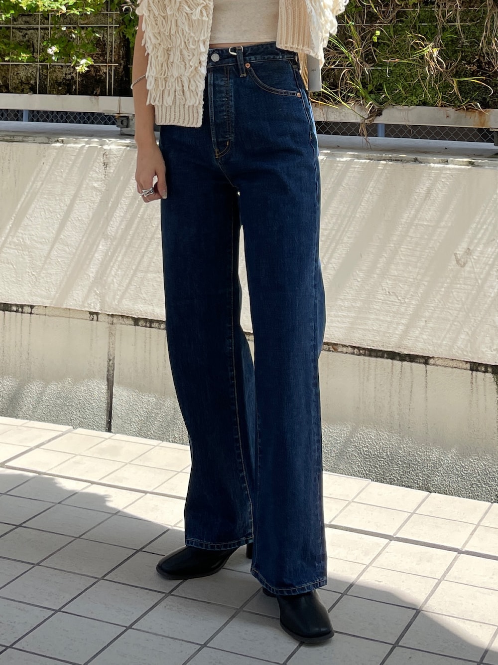 ブルー系のデニムパンツ、ホワイト系のベスト、ブラック系のブーツを着用したレディースの秋コーディネートの6枚目の写真