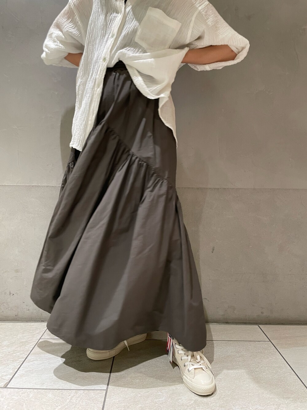グレー系のスカート、ホワイト系のスニーカー、ホワイト系のシャツ/ブラウスを着用したレディースの春コーディネートの2枚目の写真