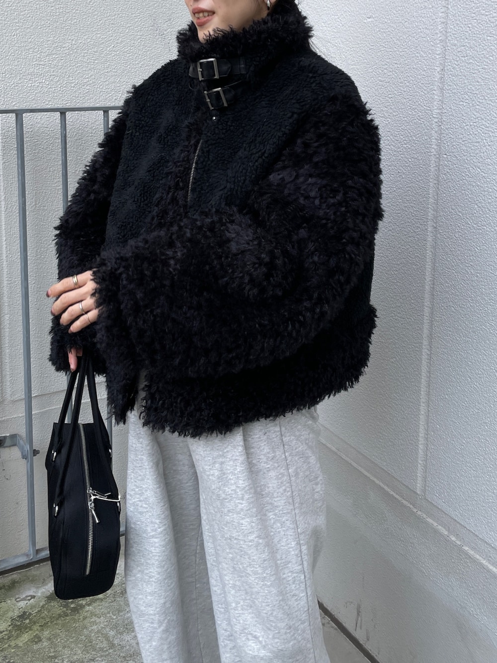 ブラック系のムートンコート、ブラック系のハンドバッグ、グレー系のスウェットパンツを着用したレディースの秋コーディネートの6枚目の写真