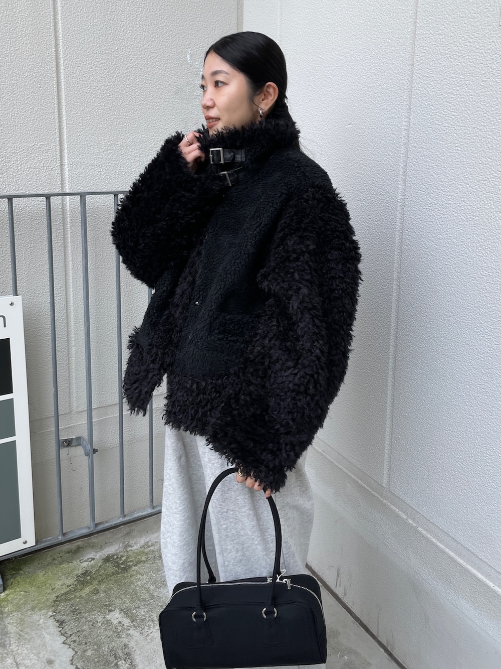 ブラック系のムートンコート、ブラック系のハンドバッグ、グレー系のスウェットパンツを着用したレディースの秋コーディネートの2枚目の写真