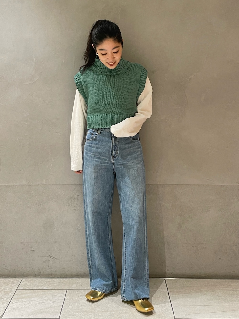 ブルー系のデニムパンツ、グリーン系のワンピース、ゴールド系のパンプスを着用したレディースの冬コーディネートの6枚目の写真