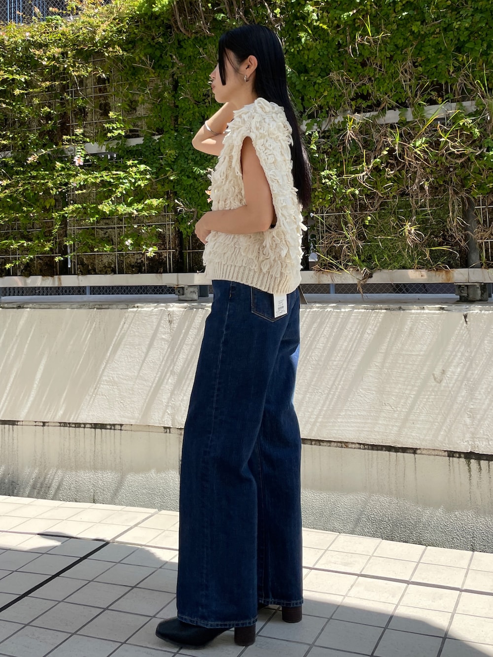 ブルー系のデニムパンツ、ホワイト系のベスト、ブラック系のブーツを着用したレディースの秋コーディネートの2枚目の写真