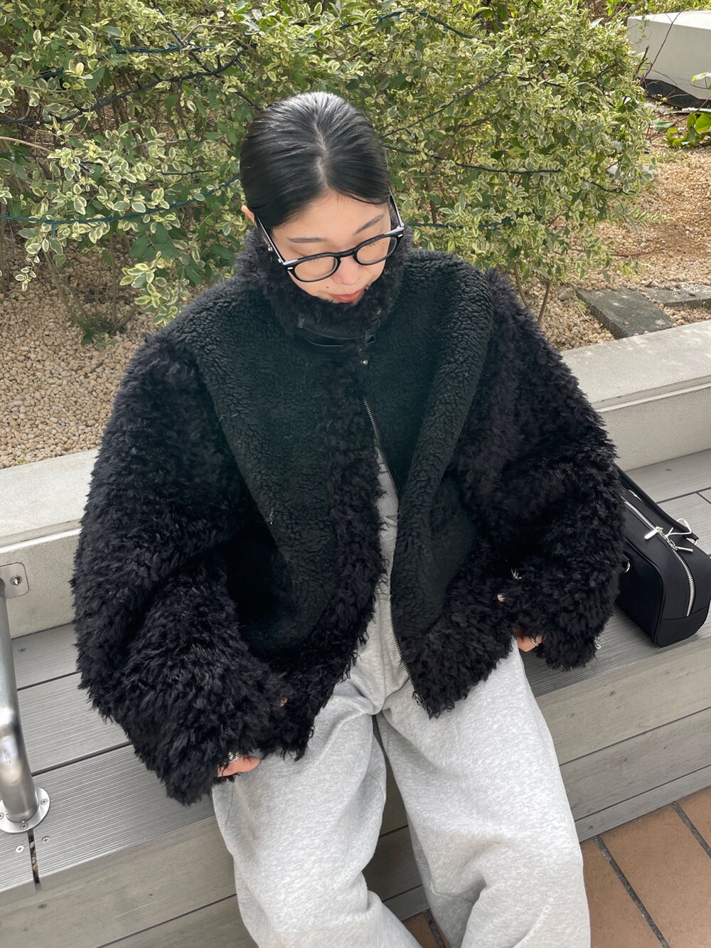 ブラック系のムートンコート、ブラック系のハンドバッグ、グレー系のスウェットパンツを着用したレディースの秋コーディネートの4枚目の写真