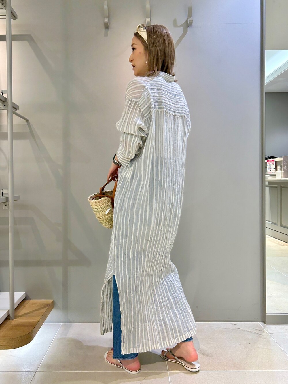 グレー系のワンピース、ブラウン系のショルダーバッグ、ブルー系のデニムパンツを着用したレディースの春コーディネートの2枚目の写真