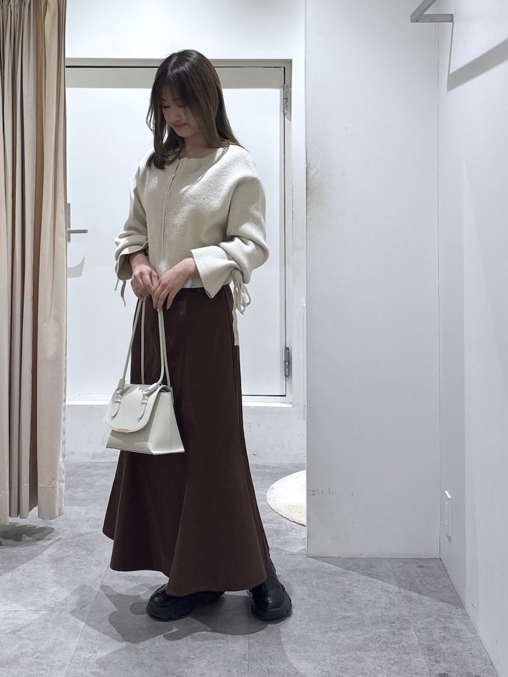 ブラウン系のスカート、ホワイト系のニット/セーター、ホワイト系のショルダーバッグを着用したレディースの冬コーディネートの2枚目の写真