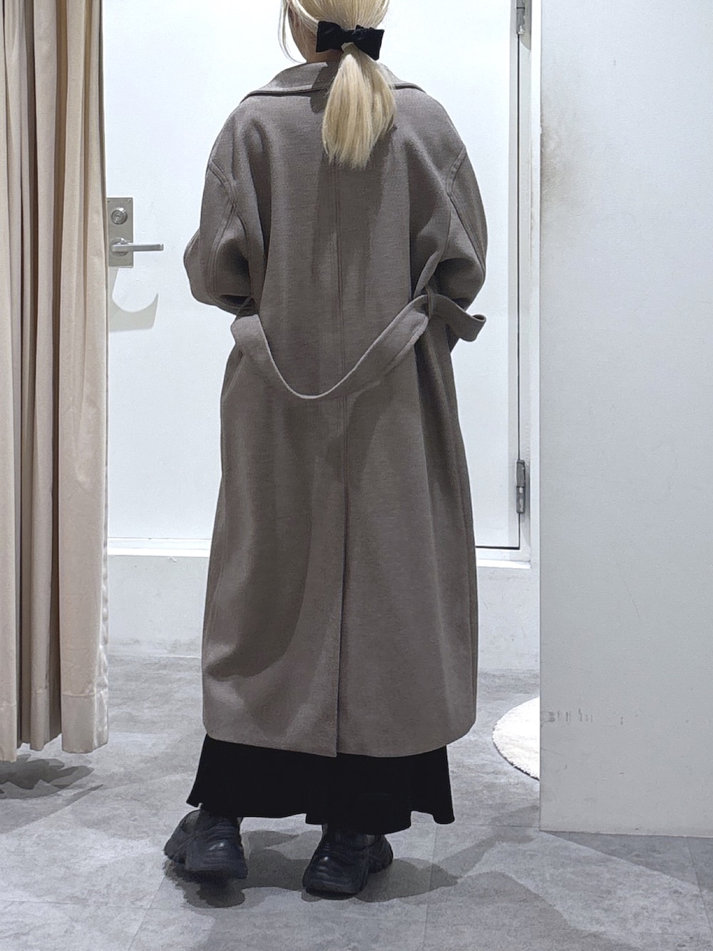 ブラウン系のステンカラーコート、ホワイト系のニット/セーター、ブラック系のスカートを着用したレディースの冬コーディネートの3枚目の写真