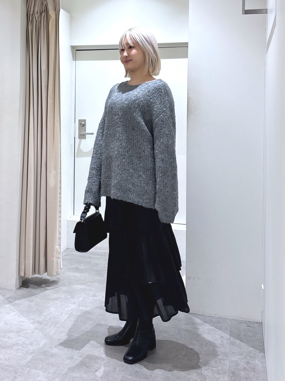 グレー系のニット/セーター、ブラック系のショルダーバッグ、ブラック系のスカートを着用したレディースの冬コーディネートの2枚目の写真