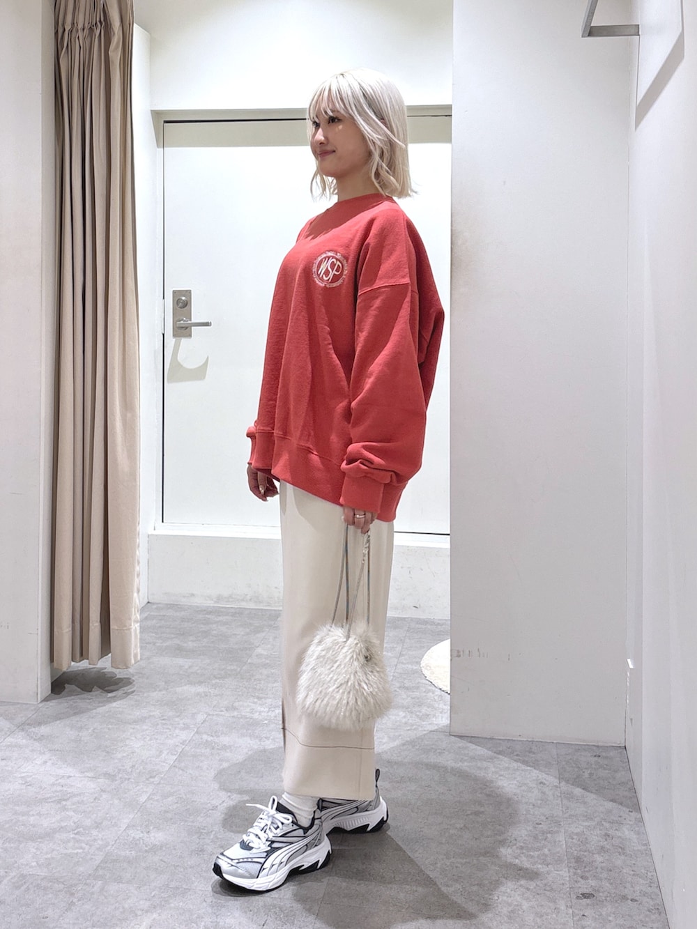 グレー系のスカート、ベージュ系のショルダーバッグ、レッド系のスウェットを着用したレディースの春コーディネートの2枚目の写真
