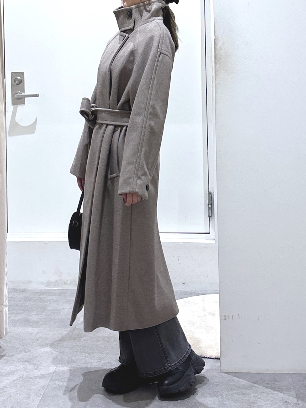 ブラウン系のステンカラーコート、ブラック系のデニムパンツ、ブラック系のショルダーバッグを着用したレディースの冬コーディネートの3枚目の写真