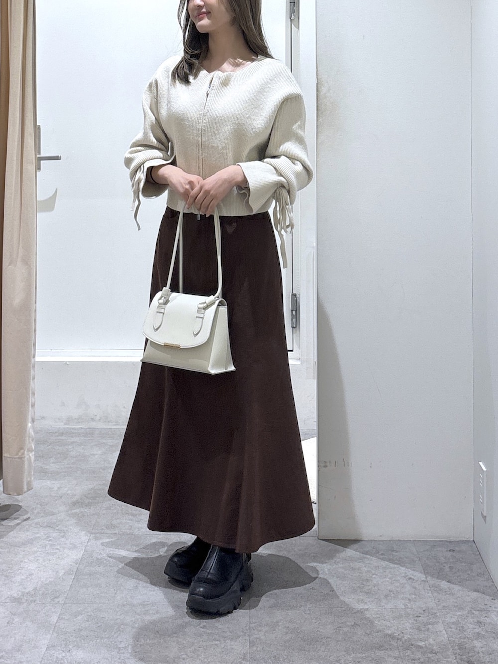 ブラウン系のスカート、ホワイト系のニット/セーター、ホワイト系のショルダーバッグを着用したレディースの冬コーディネートの3枚目の写真