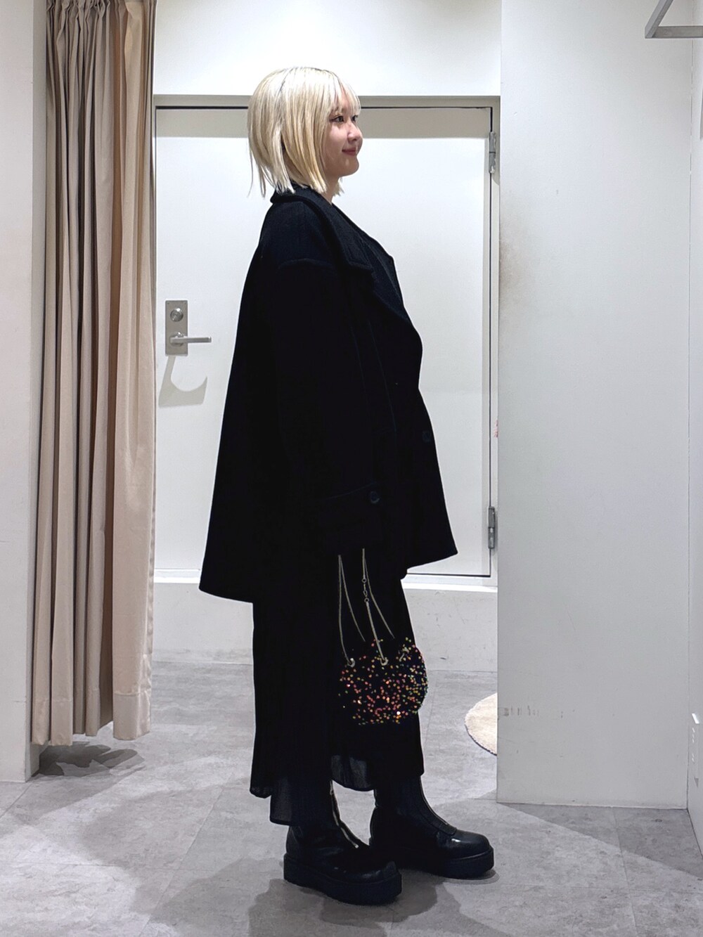 ブラック系のピーコート、ブラック系のショルダーバッグ、ブラック系のスカートを着用したレディースの冬コーディネートの3枚目の写真