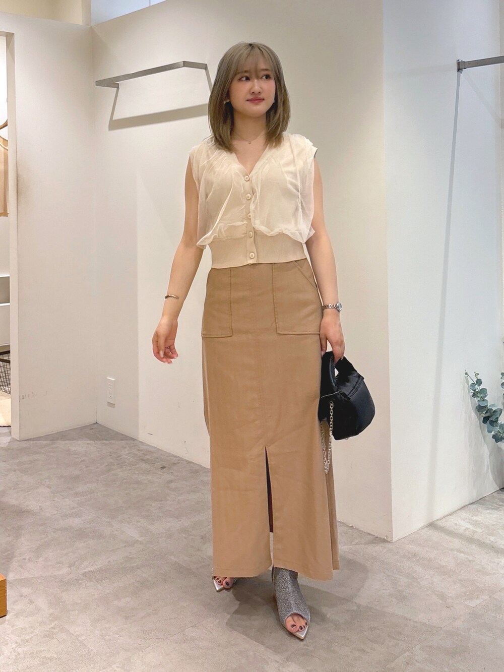 ホワイト系のベスト、ブラウン系のスカート、ブラック系のショルダーバッグを着用したレディースの夏コーディネートの2枚目の写真