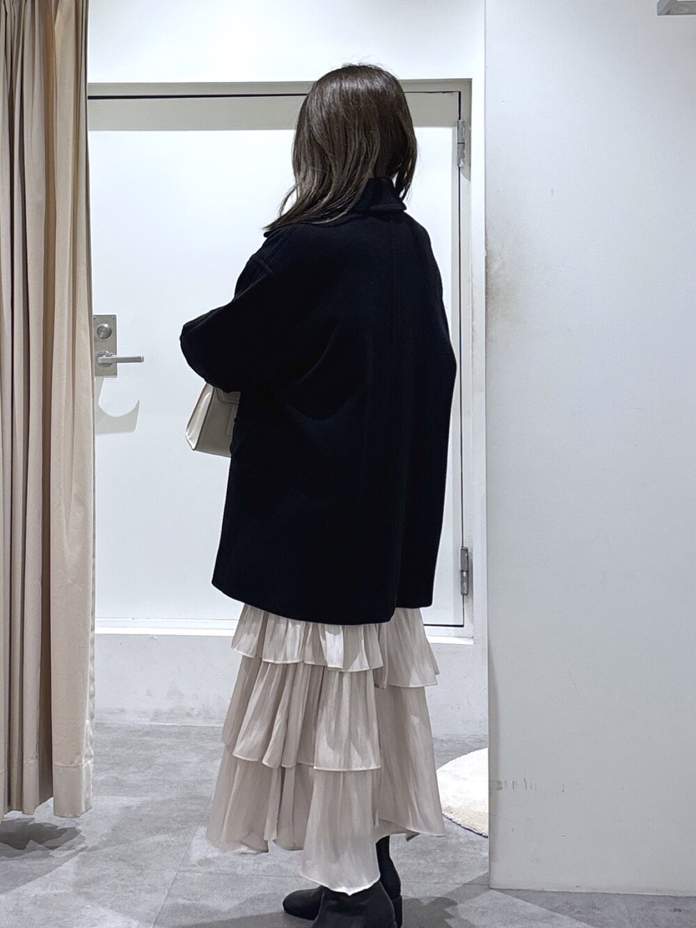 ブラック系のピーコート、ホワイト系のスカート、ブラック系のブーツを着用したレディースの冬コーディネートの4枚目の写真