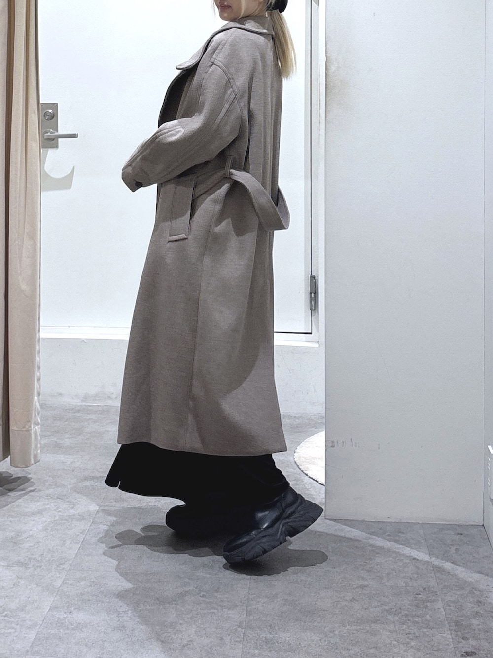 ブラウン系のステンカラーコート、ホワイト系のニット/セーター、ブラック系のスカートを着用したレディースの冬コーディネートの2枚目の写真