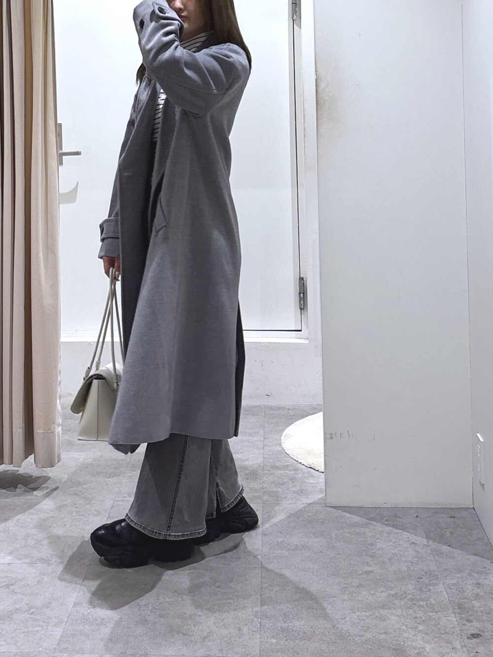 グレー系のチェスターコート、ホワイト系のニット/セーター、ブラック系のデニムパンツを着用したレディースの冬コーディネートの2枚目の写真