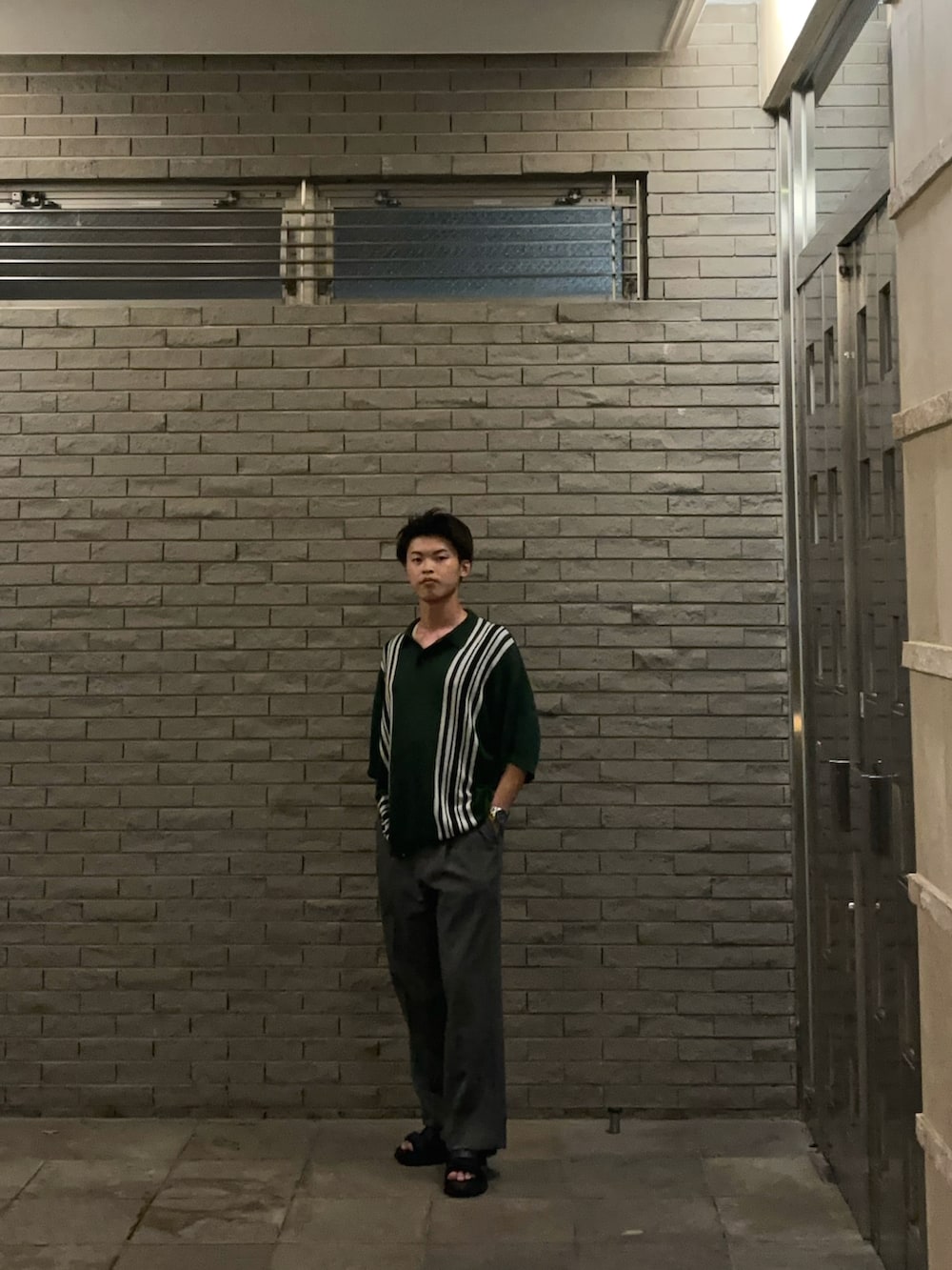 グリーン系のポロシャツ、グレー系のスラックス、ブラック系のサンダルを着用したメンズの秋コーディネートの2枚目の写真