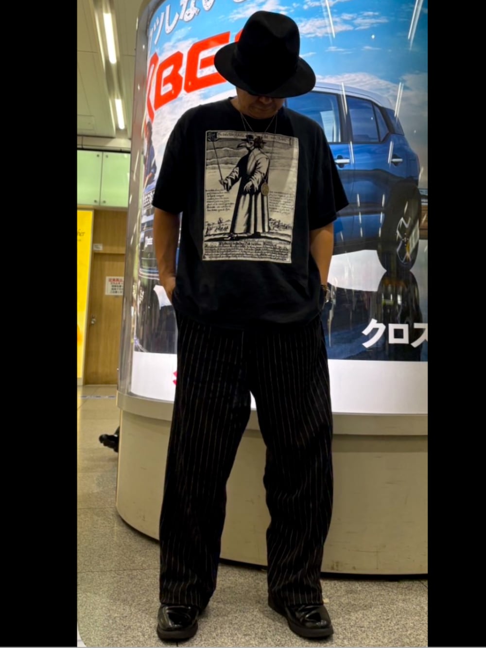 ブラウン系のトートバッグ、ブラック系のスラックス、ブラック系のTシャツ/カットソーを着用したメンズの秋コーディネートの2枚目の写真