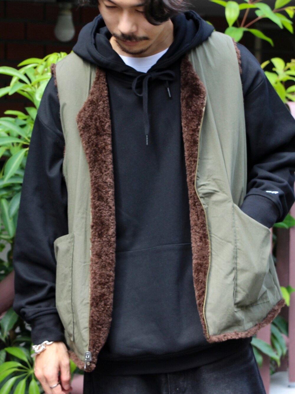 ブラウン系のベスト、ブラック系のパーカー、ブラック系のデニムパンツを着用したメンズの秋コーディネートの2枚目の写真