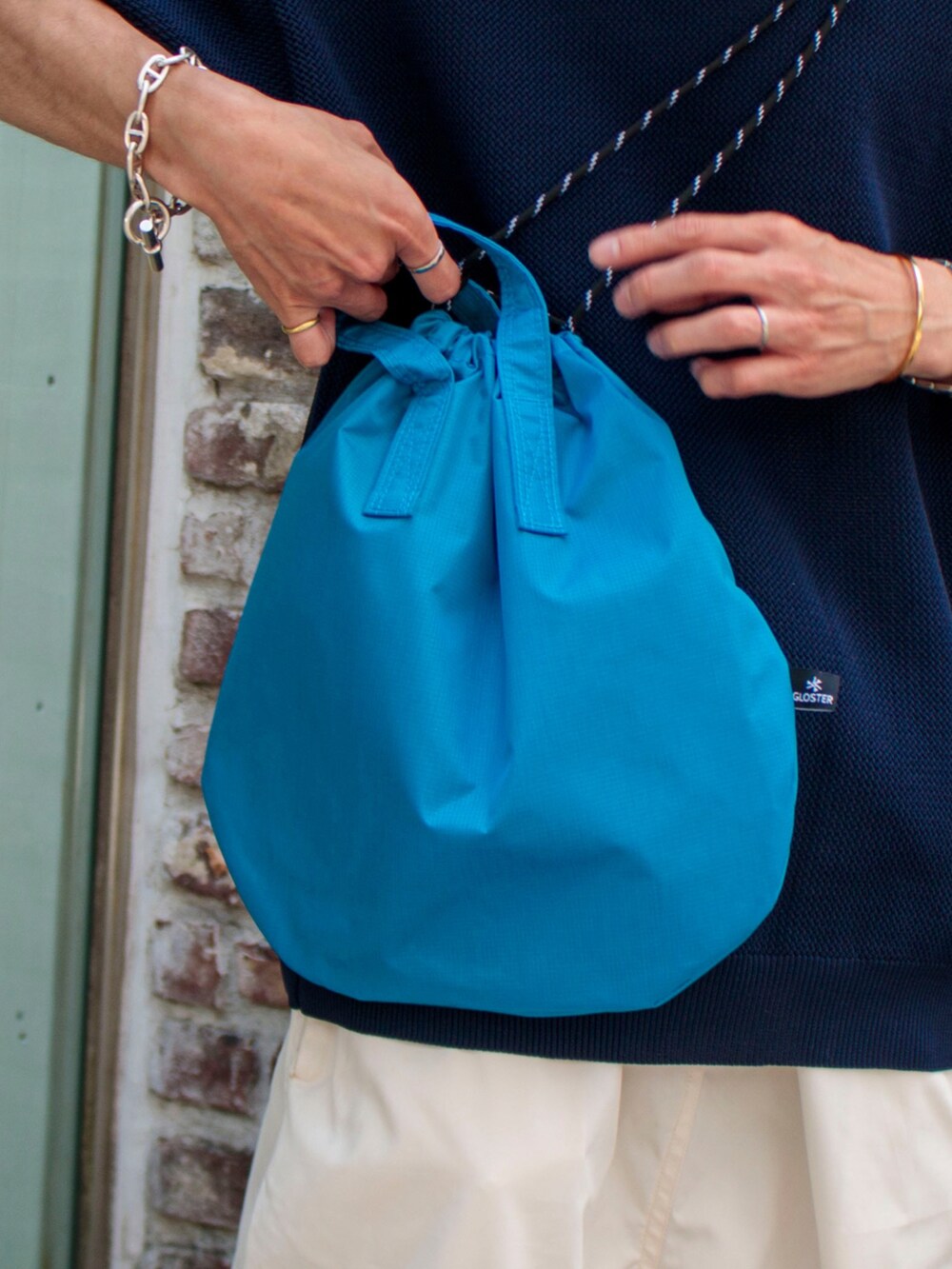 ブルー系のニット/セーター、ホワイト系のその他パンツ、ブラック系のサンダルを着用したメンズの夏コーディネートの3枚目の写真