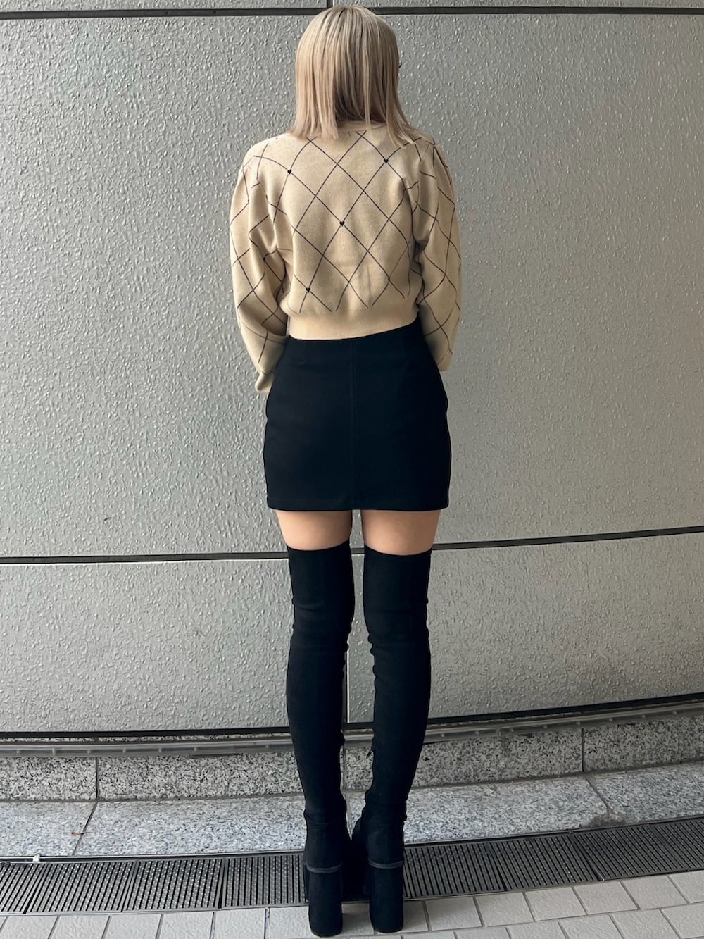 ブラック系のスカート、ベージュ系のニット/セーター、ブラック系のブーツを着用したレディースの秋コーディネートの3枚目の写真