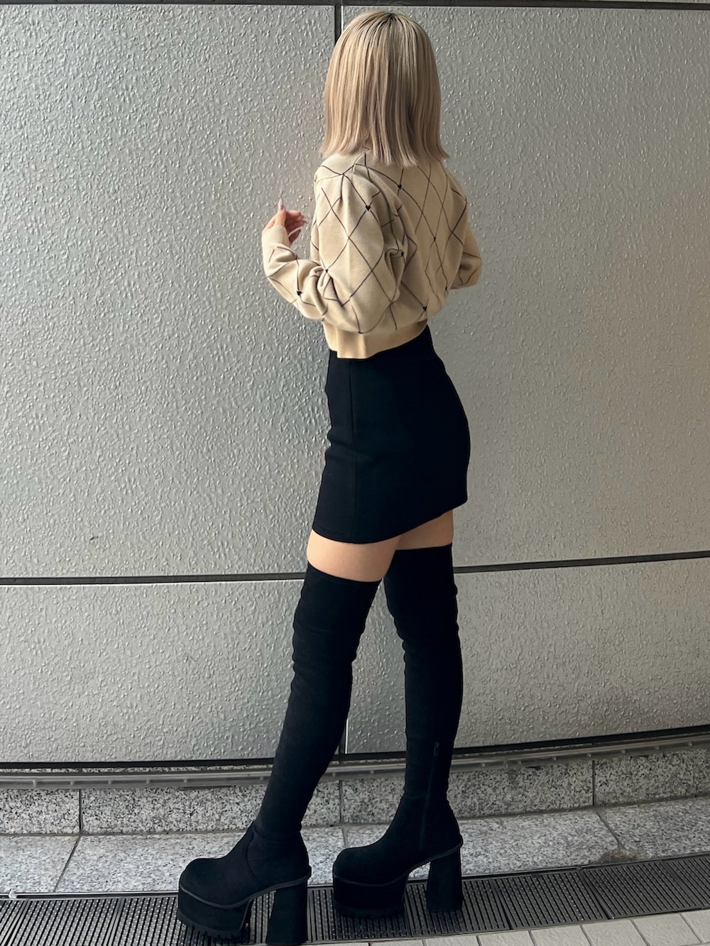 ブラック系のスカート、ベージュ系のニット/セーター、ブラック系のブーツを着用したレディースの秋コーディネートの2枚目の写真