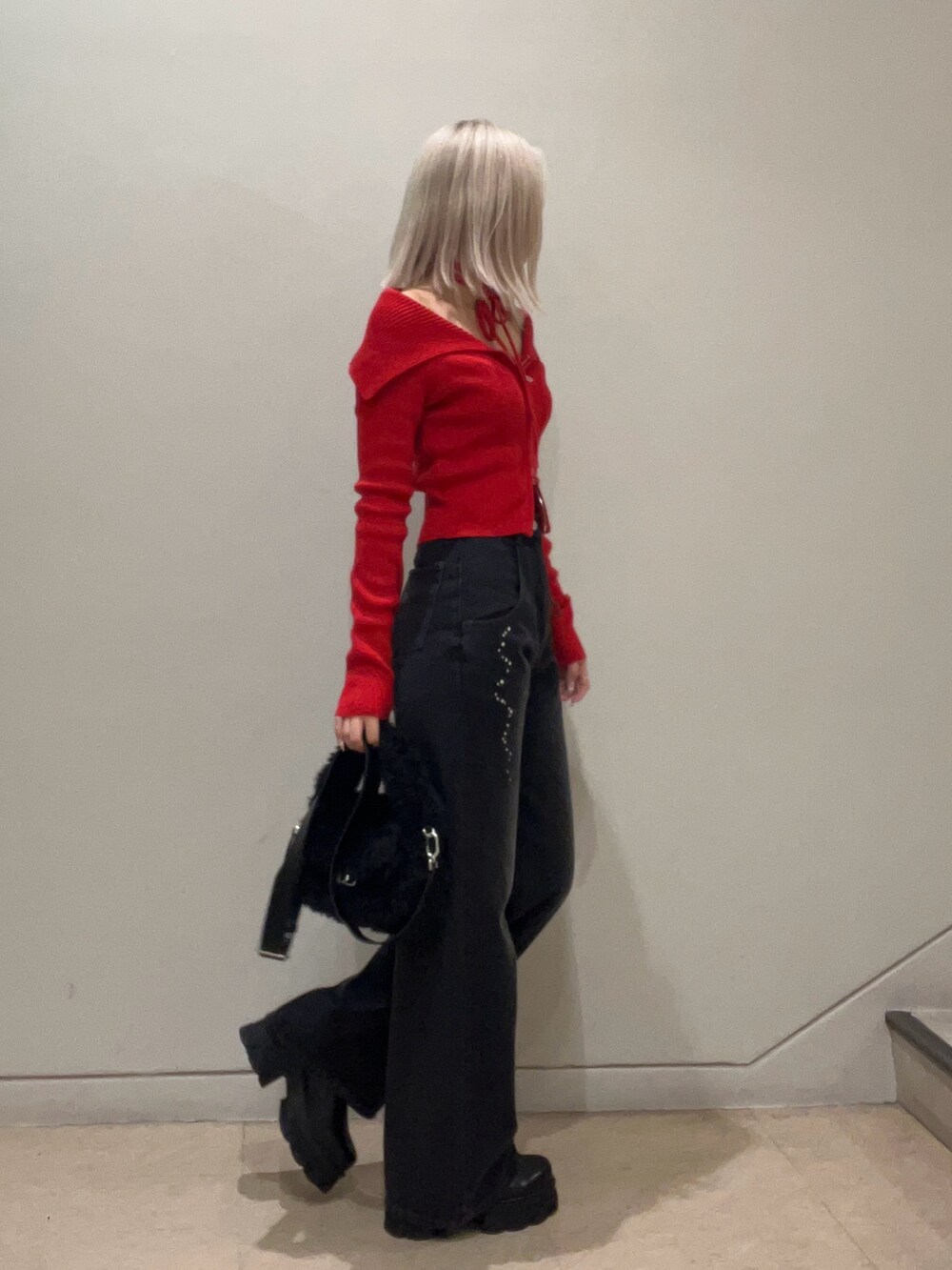レッド系のニット/セーター、ブラック系のデニムパンツ、ブラック系のハンドバッグを着用したレディースの秋コーディネートの2枚目の写真