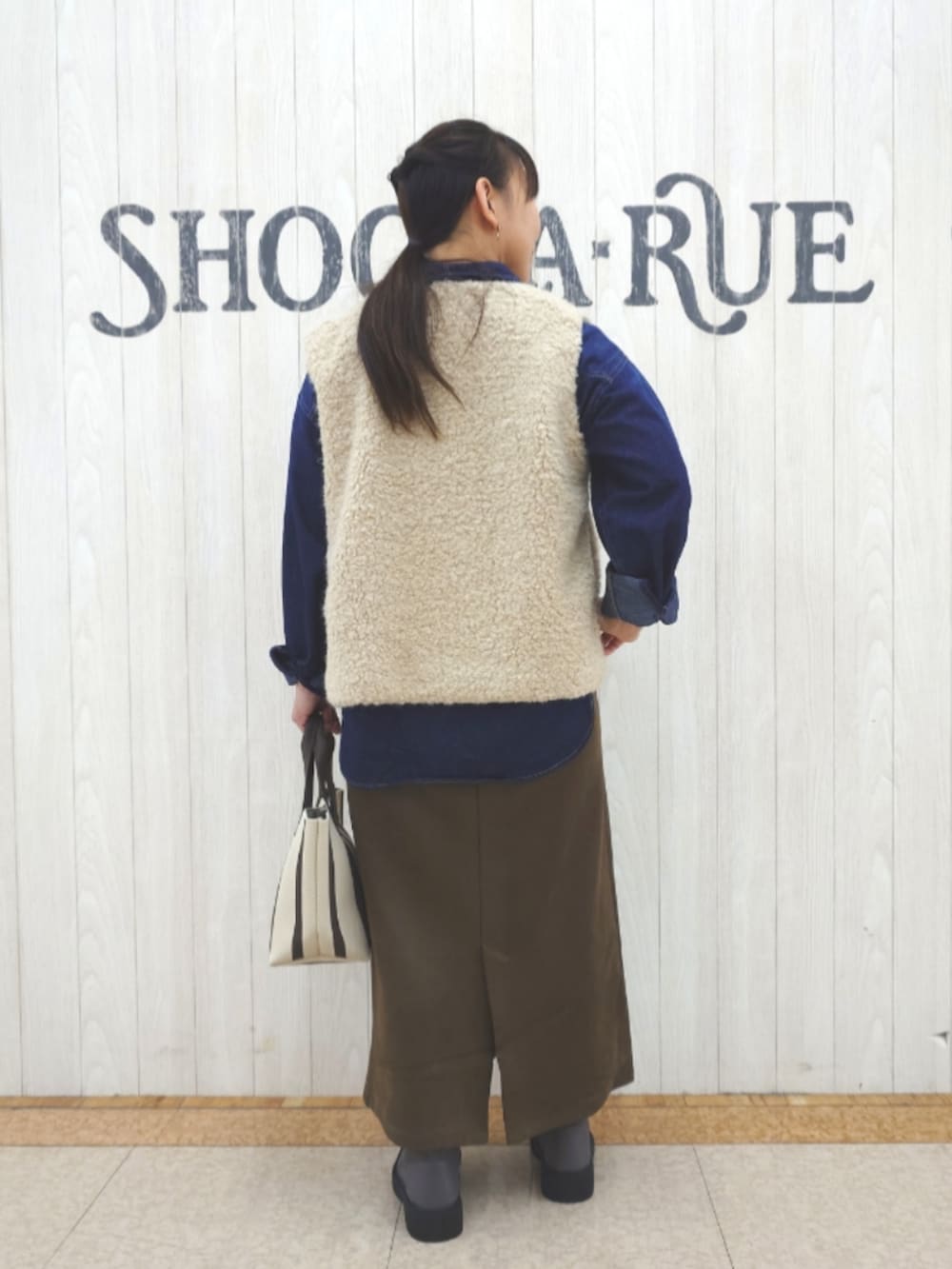 ベージュ系のベスト、ブルー系のシャツ/ブラウス、ブラウン系のトートバッグを着用したレディースの秋コーディネートの3枚目の写真